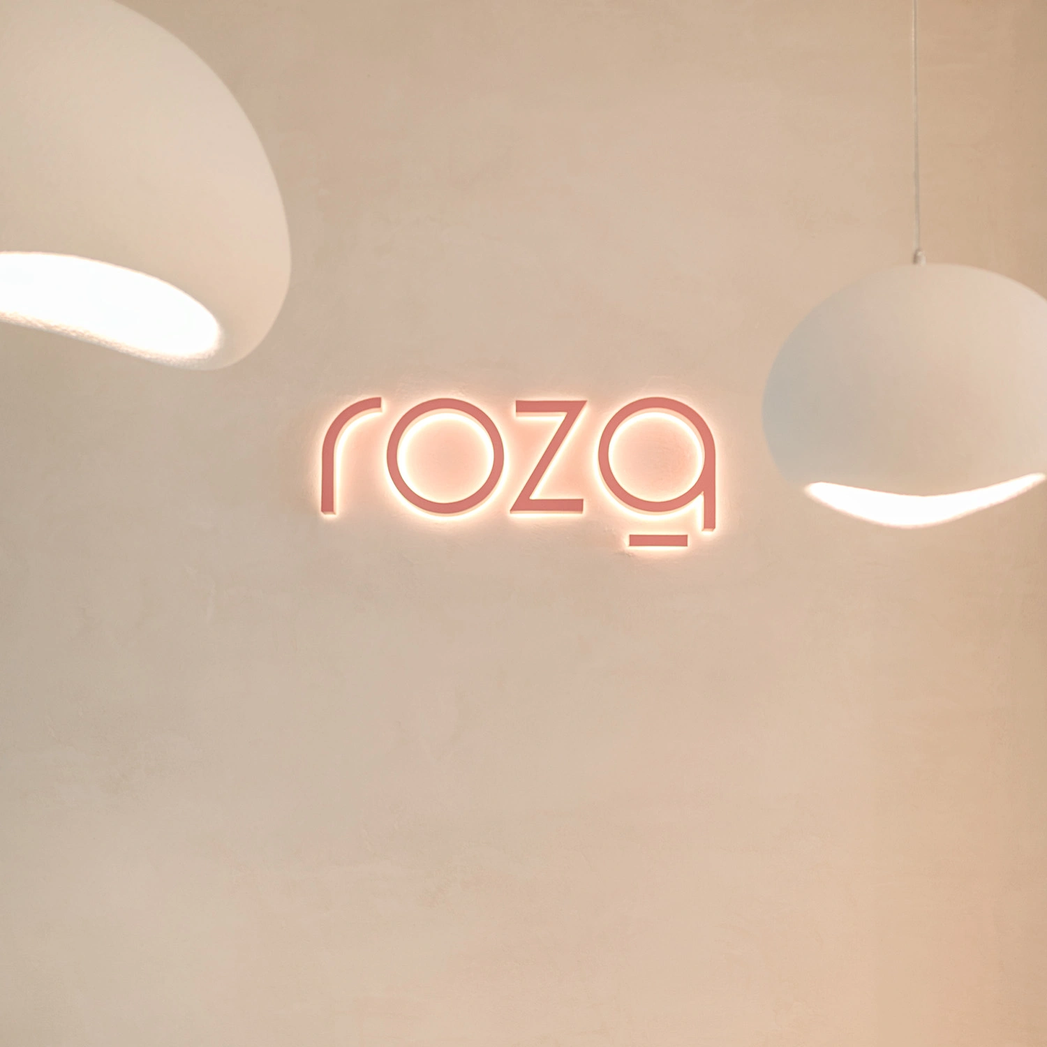 Recepción de Roza Spa Nails con el logo iluminado en la pared beige y lámparas de diseño modernas